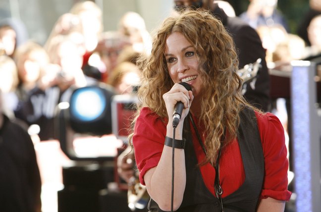 Alanis Morissette, red short-sleeved blouse, black vest, necklace, microphone